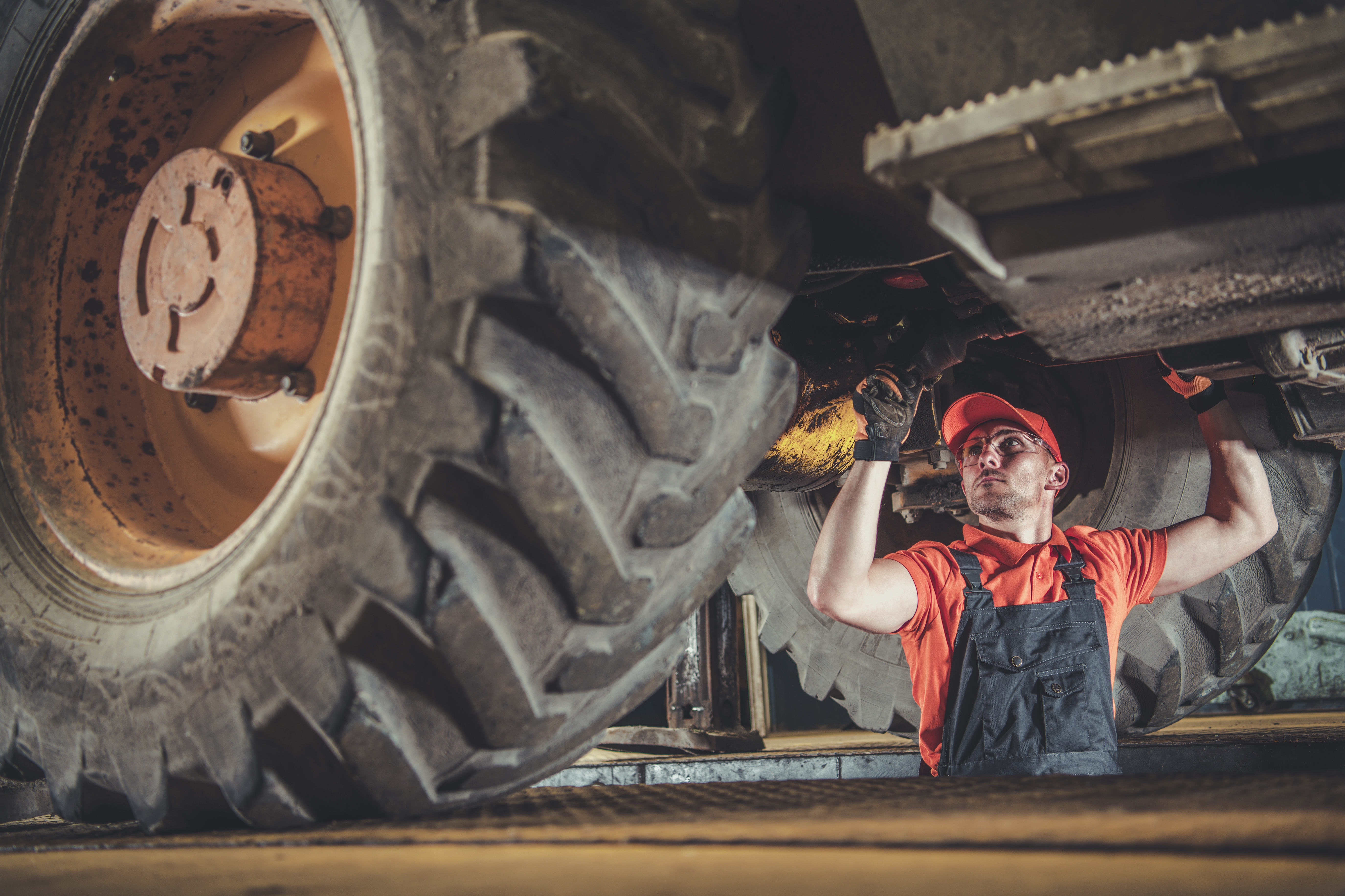 Heavy machinery mechanic working on underside of digger